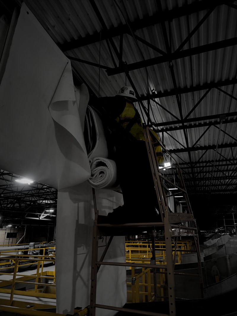 Worker on a ladder hanging white material beneath roof trusses